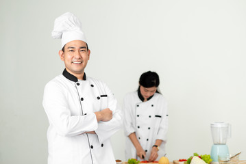 Confident Asian chef looking at camera with his helper background
