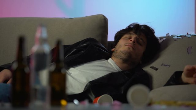 Sleepy drunk man having headache after party at home, empty bottles on table