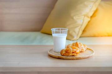 Milk and croissants serving for woman, healthy breakfast is on wooden table in bedroom in front of sofa with yellow pillows at rest area. Fresh hot bread croissants coming from baking oven.........