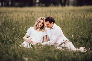 beautiful pregnant woman with her husband sitting on lawn in summer day.