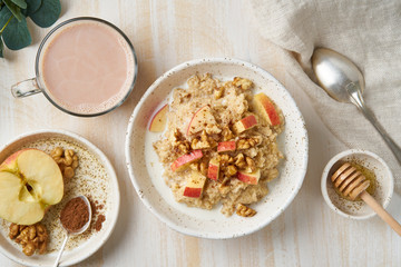 Oatmeal with apple, walnuts and cup of cocoa on white wooden light background. Top view. Healthy diet breakfast