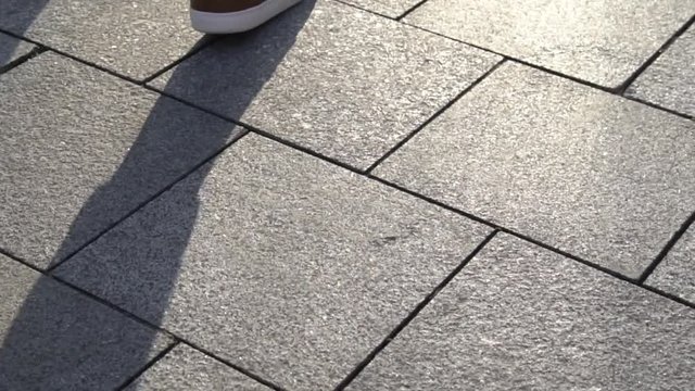 Close-up of the legs of a young man in red shoes and blue jeans walking on a city street stairs in sunny weather
