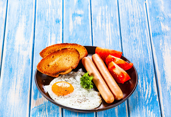English breakfast - fried egg, sausages, toasts and vegetables