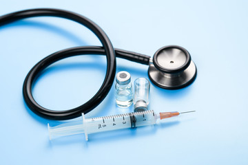 Black stethoscope and injection vaccine on blue background, medicine and drug concept