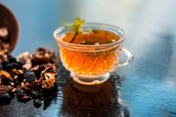 Tamarind or imli or amli in a clay bowl along with its roasted seeds and extract tea in a transparent glass cup with mint or mentha leaves on top on wooden surface.