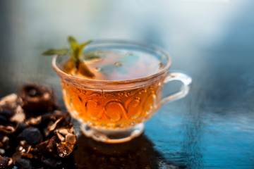 Tamarind or imli or amli in a clay bowl along with its roasted seeds and extract tea in a transparent glass cup with mint or mentha leaves on top on wooden surface.