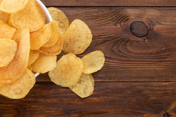 Crispy potato chips in bowl on wooden background, top view