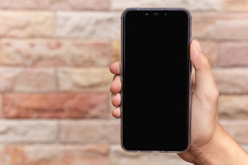 Man holding black smart phone with stone Cladding wall background.