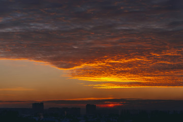 Cityscape with vivid fiery dawn. Amazing warm dramatic cloudy sky above dark silhouettes of city...