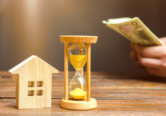 Wooden house and clock. Businessman counting money. Payment of deposit or advance payment for...