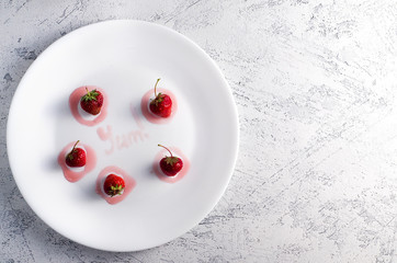 Strawberries in a white plate and yum typography made with jam. Top view