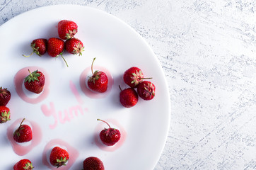 Strawberries in a white plate and yum typography made with jam. Top view