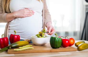 Obraz na płótnie Canvas Smiling pregnant woman eating vegetables salad for health, close up