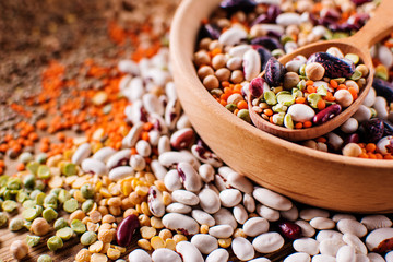 Mixed raw legumes, pulses in a wooden spoon, closeup view with details