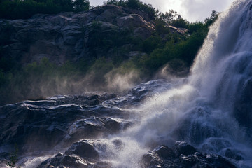 The rays of the sun through the clouds illuminate the spray from the waterfall.