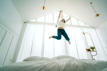exited asian woman jump over white bed in bedroom with energy and happiness success lifestyle ideas concept - Powered by Adobe