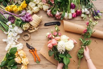 Partial view of florist making flower bouquet on wooden surface