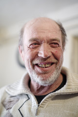 Portrait of a smiling elderly man. Unshaven man with bad teeth at home