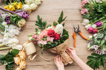 Cropped view of florist making flower bouquet on wooden surface