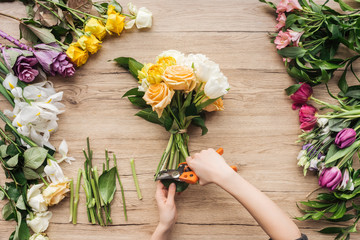 Cropped view of florist cutting flower stalks in bouquet on wooden surface