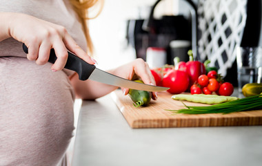Pregnant woman preparing salad and cutting vegetables in kitchen