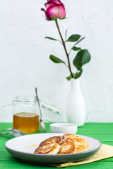 Ready-to-eat sweet cottage cheese pancakes with honey  on a plate and rose in a vase on a wooden table
