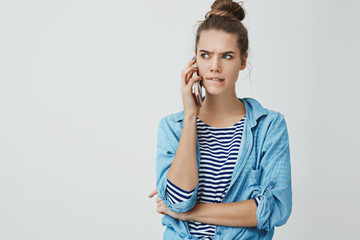 Girl facing tough troublesome choice perplexed biting lower lip frowning looking seriously aside holding smartphone talking having hard conversation, thinking, taking decision, white background