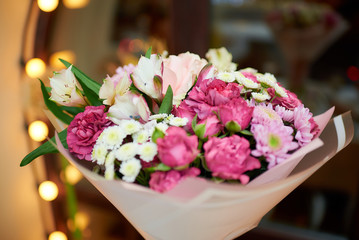 Bouquet of pink, white, violet flowers near the window with yellow light bulbs in a restaurant. Chrysanthemums, roses, daisies, daisy, chain, daisy wheel, chamomile together