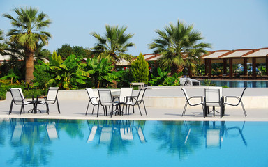 Woman in a straw hat relaxing on a daybed near a luxurious summer pool, concept time to travel.