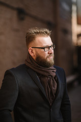 Fototapeta premium A man with a beard in a black warm coat with a scarf poses to advertise men's clothing in the winter. Advertise men's clothing