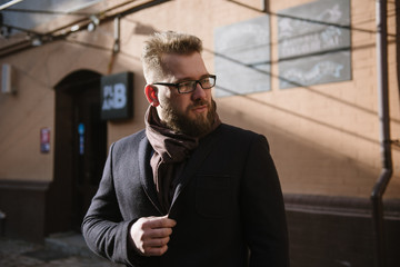 A man with a beard in a black warm coat with a scarf poses to advertise men's clothing in the winter. Advertise men's clothing