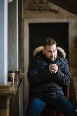 Obraz premium A man with a beard in a warm winter jacket poses for advertising men's clothing in the winter. Advertising of men's clothing