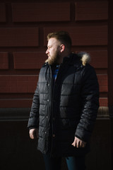 A man with a beard in a warm winter jacket poses for advertising men's clothing in the winter. Advertising of men's clothing