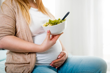 Happy pregnant woman at home eating vegetable salad at home