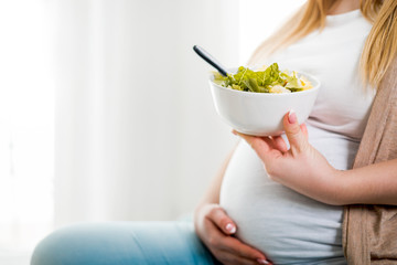 Happy pregnant woman at home eating vegetable salad at home