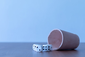 Brown lether yahtzee cup lying beside some white dices on a wooden table