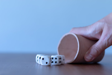 Hand of a men playing yahtzee with brown leather cup and dices