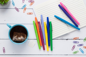 colorful pens on a wooden tabletop with a notebook