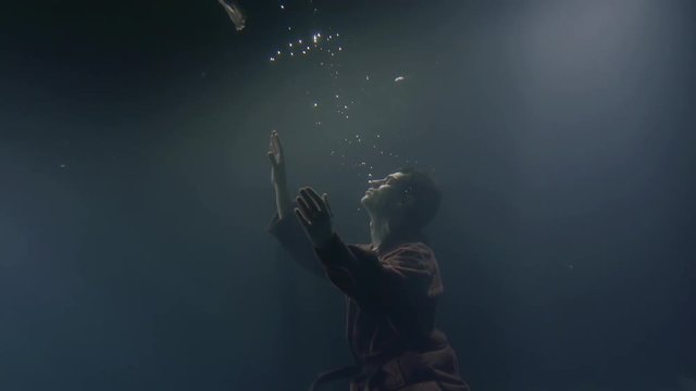 drowning man is stretching hands up to surface of sea, underwater shot