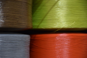 Large bobbins of polypropylene yarn. Large reels Orange, Pink and Red yarns, close up, selective focus. Fragment of bobbins of red and green thread