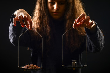 Emotional portrait of a girl with long curly hair weighing grain and weights on scales against a black background