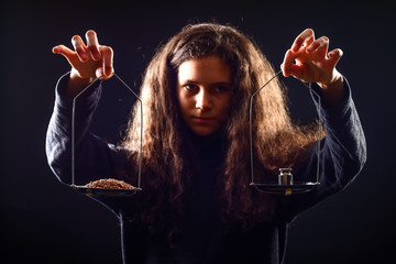 Emotional portrait of a girl with long curly hair weighing grain and weights on scales against a black background