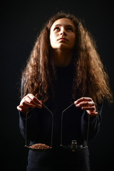 Emotional portrait of a girl with long curly hair weighing grain and weights on scales against a black background