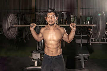 Fototapeta na wymiar portrait of a handsome athlete at gym. man does the exercise with a barbell, standing and squatting. big confident muscular man training. motivation. muscles. - Image