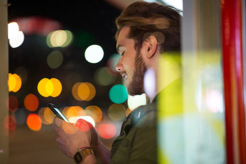 Young man using smartphone on urban street at night