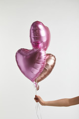 partial view of girl holding heart-shaped pink air balloons isolated on white
