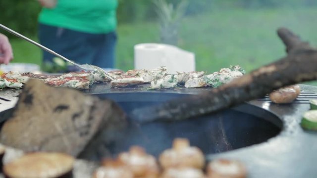 Healthy summer food. Assorted delicious grilled meat with vegetable over the coals on a barbecue. Chef turns the pieces of meat on a hot grill. Happy people having camping and bbq party outdoor.