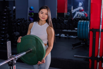 Girl adds weight to the bar. Asian woman adding weight on a bar as she workout in fitness gym