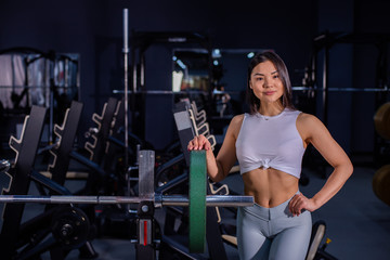 Fototapeta na wymiar Girl adds weight to the bar. Asian woman adding weight on a bar as she workout in fitness gym
