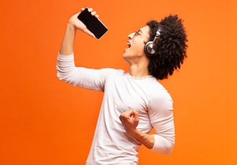 Young emotional black man singing his favorite song on smartphone
